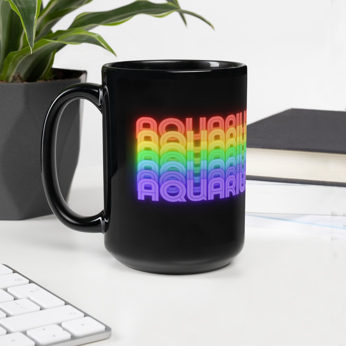 Black mug with colorful 'Aquarius' design on a desk with a plant and books in the background (15 oz.)